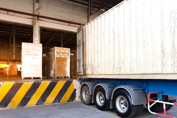 A semi-truck backed up to a loading dock with pallets of cargo being prepared for transport.