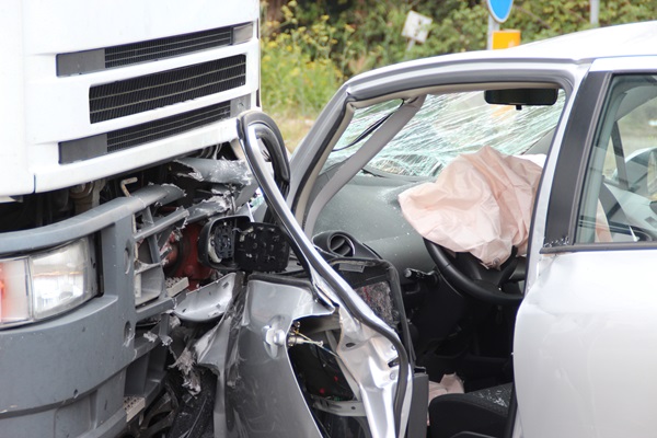 Silver car with deployed airbags heavily damaged in a head-on crash with a large white semi-truck on an Indiana road.