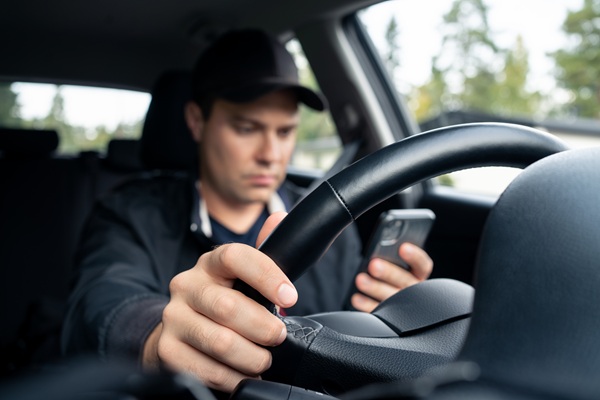 A driver in a baseball cap looking down at a smartphone while holding the steering wheel, illustrating the dangerous behaviors targeted during Indiana law enforcement crackdowns on distracted driving and speeding.